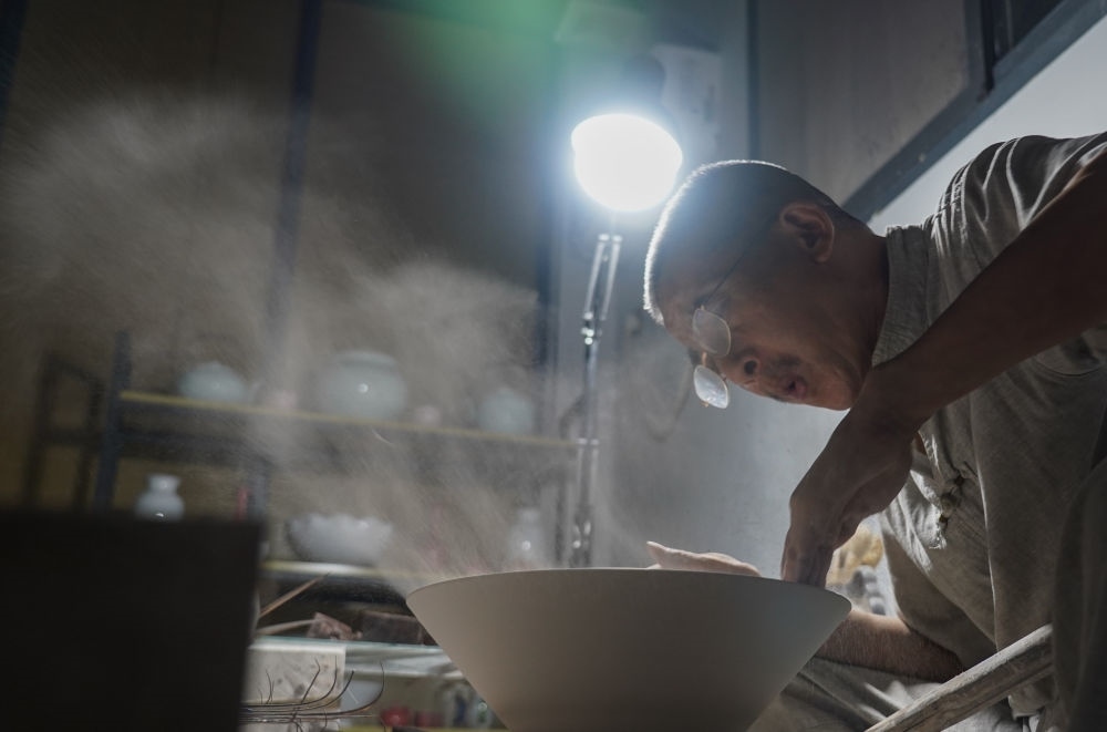 ↑ 在景德鎮(zhèn)，手工匠人吹去坯內(nèi)的泥土（2021年7月14日攝）。