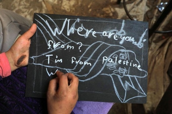 2023年12月28日，一名學(xué)生在加沙地帶南部城市拉法一所學(xué)校的臨時教室中寫下“我來自巴勒斯坦”的字樣。新華社發(fā)（里澤克·阿卜杜勒賈瓦德攝）