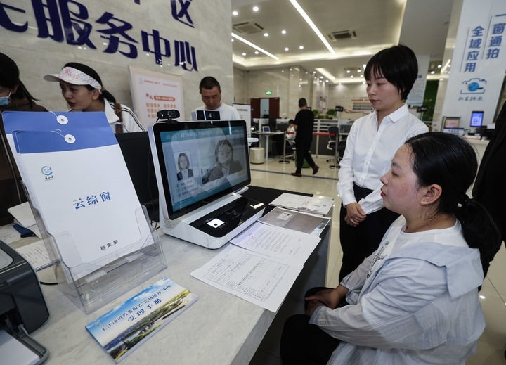 在浙江省嘉興市秀洲區(qū)王江涇鎮(zhèn)便民服務(wù)中心的“跨域通辦·云綜窗”窗口，辦理開業(yè)登記的個體工商戶（右一）通過該系統(tǒng)與江蘇省蘇州市吳江區(qū)盛澤鎮(zhèn)行政審批局工作人員視頻連線，進行身份讀取及材料線上審核（2024年5月9日攝）。新華社記者 徐昱 攝