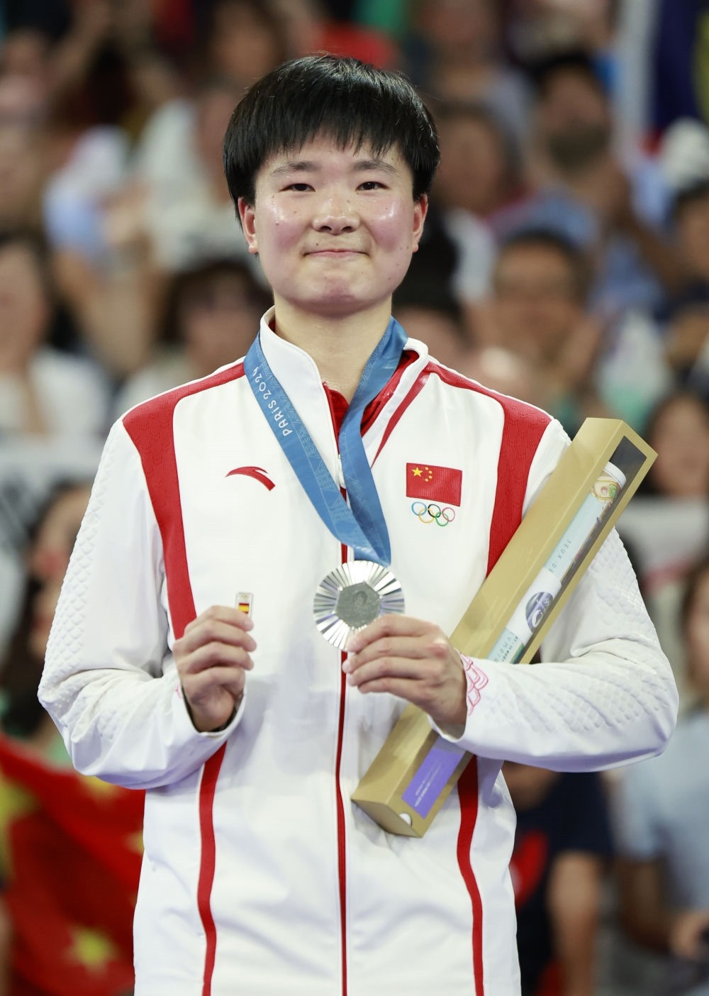 巴黎奧運(yùn)會(huì)羽毛球女子單打亞軍、中國(guó)選手何冰嬌在頒獎(jiǎng)儀式上一手握著銀牌，一手握著西班牙奧委會(huì)徽章（2024年8月5日攝）。新華社記者 任正來 攝